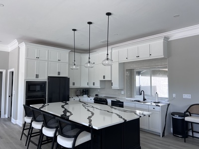 Modern kitchen with white cabinets, a large island with a white and black marble countertop, four bar stools, black appliances, and three hanging pendant lights.