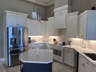 Modern kitchen with white cabinetry, stainless steel appliances, a central island, and a tiled backsplash. The space is well-lit with under-cabinet lighting and a contemporary pendant light.