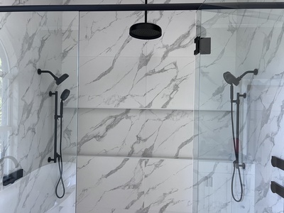 A modern bathroom features a glass-enclosed shower with white and gray marble walls, dual black showerheads, and sleek black fixtures.