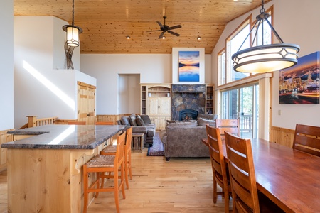 Alternative View showing the open floor plan with the grand rock fireplace anchoring the room.  Beautiful pine hardwood floors are featured throughout!  Peek view of top of staircase that leads down to the entrance and lower level of the home. 