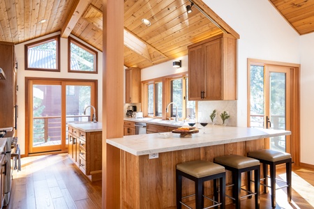 Natural stone counters,  island with sink, large sliding glass door leading to deck, wide breakfast counter w/seating, cathedral ceiling, and skylight, recessed and track lighting that provides warmth and light from the natu