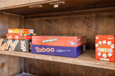 A wooden shelf holding several boxed games, including Jenga, Scattergories, Taboo, and Farkle.