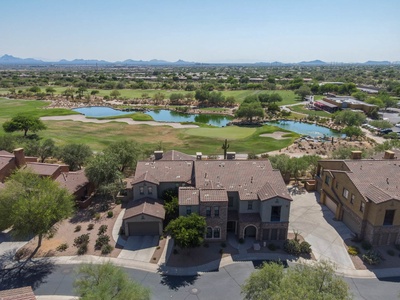 Aerial view of a residential neighborhood with houses, a golf course, water features, and a distant mountain range under a clear sky.