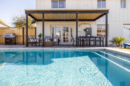 A backyard features a covered patio with seating, dining table, and grill