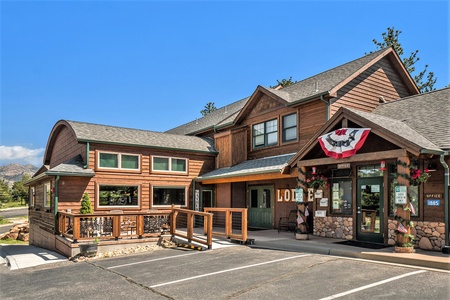 A rustic wooden lodge with an accessible ramp, decorated with potted flowers and a patriotic flag banner near the entrance.