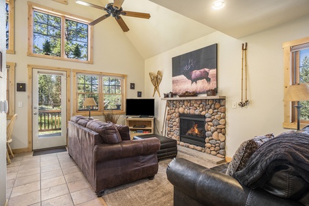 Living room with sofa that seats 3, ottoman, love seat that seats 2, ceiling fan, fireplace, and flat screen TV.