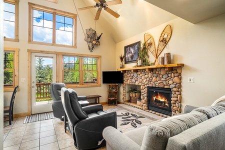 Living room with 2 leather recliners, sofa that seats 3, fireplace, flat screen TV, vaulted ceiling, ceiling fan, windows with mountain views, and patio door to deck.