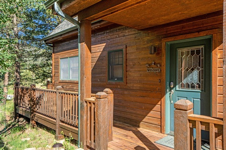 Exterior of cabin, with small porch that wraps around to deck, and front door.