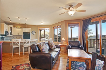 Living room with leather sofa and chair opens into kitchen with seating at the breakfast bar.