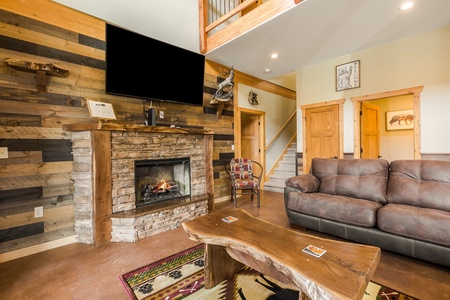 The living area features a large flatscreen TV, a fireplace, rustic wooden accent furniture, and comfy couches