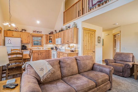 Living room adjacent to the kitchen, with sofa that seats 3, arm chair, and kitchen.