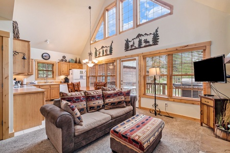 Living room sofa with seating for 4, and ottoman, flat screen TV. Kitchen area with dining table with seating for 6, and views of outdoors.