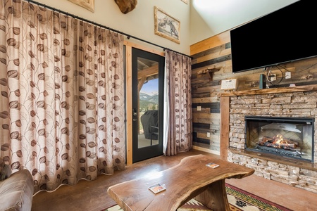 The living area features a large flatscreen TV, a fireplace, rustic wooden accent furniture, and comfy couches