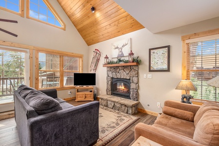 Living room with vaulted ceiling, fireplace, flat screen TV, sofa that seats 3, love seat that seats 2.