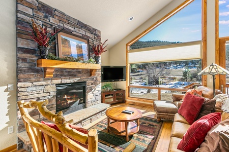 Large open living with plenty of comfy seating for all, floor to ceiling windows with a river view, and cozy gas fireplace.