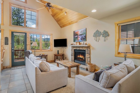 Living room with vaulted ceiling, ceiling fan, sofa that seats 3, loveseat that seats 2, coffee table, flat screen TV, fireplace, and windows with view of mountains.