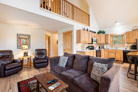 Living room with sofa that seats 3, coffee table, 2 leather arm chairs, end table with lamp, with view of loft and kitchen areas.