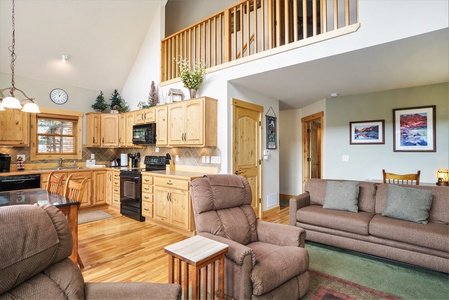 Open concept kitchen and living room, with loft overhead. Living room with sofa that seats 4, 2 reclining chairs with end table.