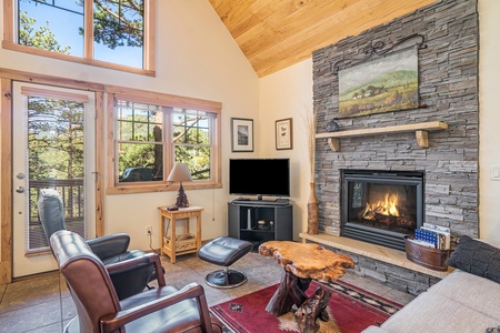 Living room with vaulted ceiling, sofa that seats 3, coffee table, two chairs, flat screen TV and fireplace.