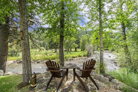 Elk River Cabin Adirondack chairs on riverbank in backyard.