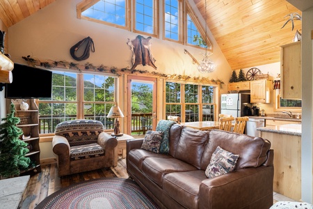 Living room with flat screen TV , leather couch that seats 3, armchair, kitchen area, and mountain views.