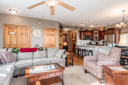 Open concept living room, kitchen. Bar seating with stools in kitchen area. L shaped sofa and oversized chair in living room. 