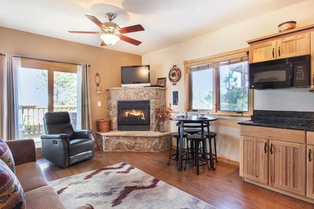 Open living/dining area with stone gas fireplace, bar height table with seating for four, lazy boy recliner and queen sleeper sofa.