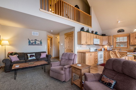 Open concept living room/kitche, with loft overlooking living area, sofa that seats 3, coffee table, floor lamp, 2 recliners, and end table.