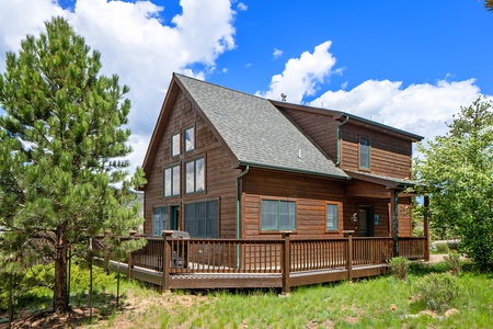 Exterior view of cabin, with large deck with porch that wraps around to front door.