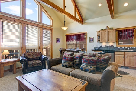 Open concept living/dining room area with floor-to-ceiling windows boasting mountain views that can be enjoyed from the queen sleeper sofa or oversize chair. 