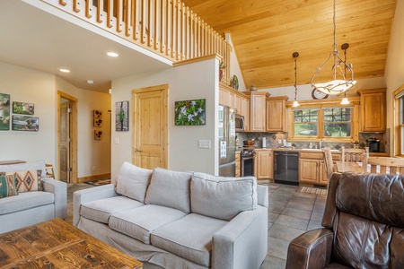 Living room with vaulted ceiling, sofa that seats 3, loveseat that seats 2, leather arm chair, coffee table, and kitchen.