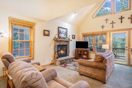 Living room with vaulted ceiling, sofa that seats 3, fireplace, flat screen TV, 2 arm chairs and end table.