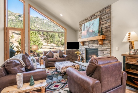 Main floor living room with ample sofa seating, gas fireplace, and a serene view out to the deck. Townhome is adorned with charming mountain decor.