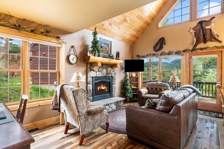 Living room with fireplace, flat screen TV, leather couch, two arm chairs, and view of the mountains.