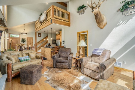 Elk River Cabin Living room with love seat that seats 2 and ottoman, 2 arm chairs, side table with lamp, and loft area overhead.