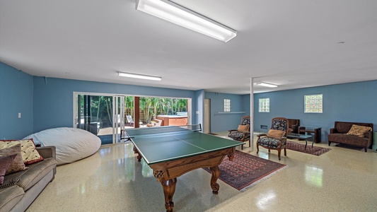Spacious game room with a ping pong table which opens to billiards table, lounge seating, and sliding glass doors that open to a backyard with a hot tub.