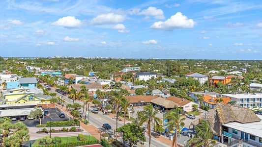 Aerial view of a suburban area with a mix of residential housing, commercial buildings, trees, and clear blue sky with scattered clouds.