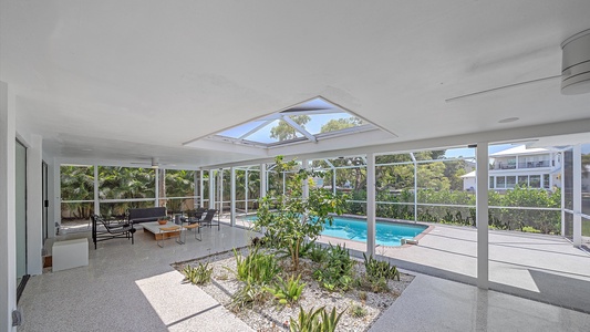 Spacious indoor patio with skylight, seating area, indoor plants, and view of an outdoor pool through large windows.