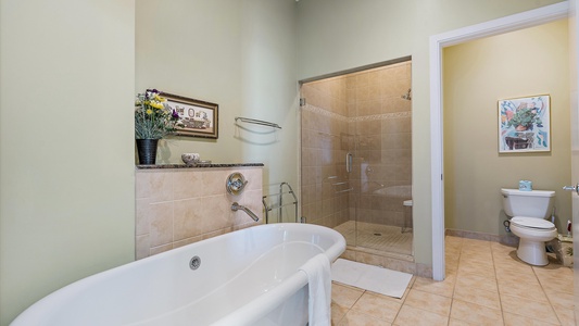 A bathroom with a standalone bathtub, a walk-in shower, and a toilet. A towel hangs on the tub, and a picture and decorative items are displayed on the wall shelf above the tub.