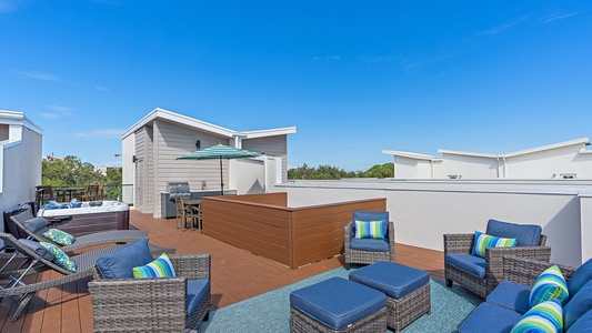 Rooftop patio with wicker furniture, blue cushions, striped pillows, a rug, a table with chairs, and an umbrella.