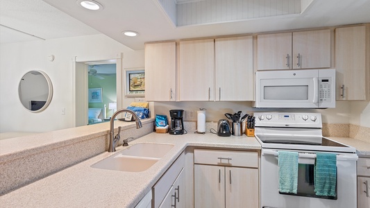 Modern kitchen with beige cabinets, white appliances, a double sink, and a granite countertop. Small kitchen appliances including a coffee maker, toaster, and knife set are on the counter.