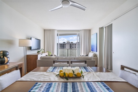 A modern living room with a ceiling fan, light-colored furnishings, a smart TV on the wall