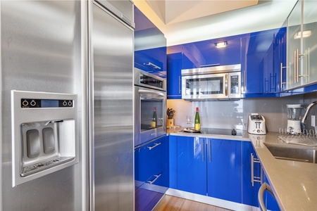 Modern kitchen with Italian blue cabinets, stainless steel refrigerator, microwave, oven, and countertop appliances such as a blender and toaster.