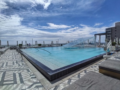 Rooftop swimming pool with clear blue water, submerged stairs, and lounge chairs