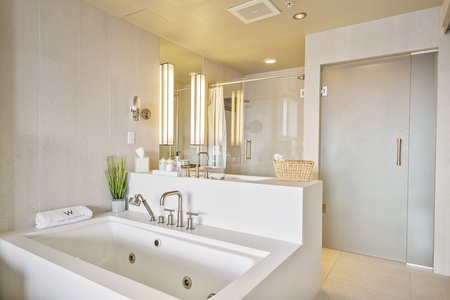 A modern bathroom features a white bathtub, wall-mounted faucet, glass shower door, toiletries and illuminated mirror.