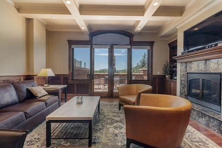 A cozy living room with leather furniture, a wooden coffee table, a fireplace, and a large window with a view of an outdoor patio.