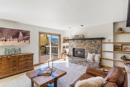 Beige couch, brown leather couch, television behind decretive sliding mural, fireplace, square coffee table, sliding glass door exiting onto porch.