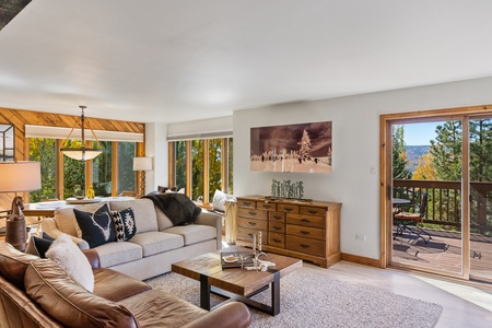 Beige couch, brown leather couch, television behind decretive sliding mural, fireplace, square coffee table, large windows in dining room overlooking Yampa Valley