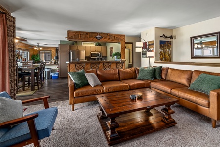 A spacious living room with a brown leather sectional sofa, wooden coffee table, and an open view of the adjacent kitchen and dining area.