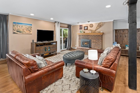 Brown couches, grey ottoman, TV, large windows.